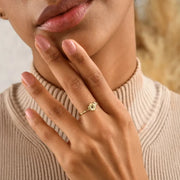 Close-up of a hand wearing a 14k gold filled cut out ring with a flower design, against a neutral background.